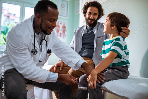 Pediatrician checking reflexes of a young boy in a medical clinic with his father present photo