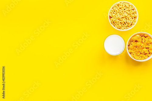 Various corn cereals in bowls and milk on yellow background top view copyspace photo