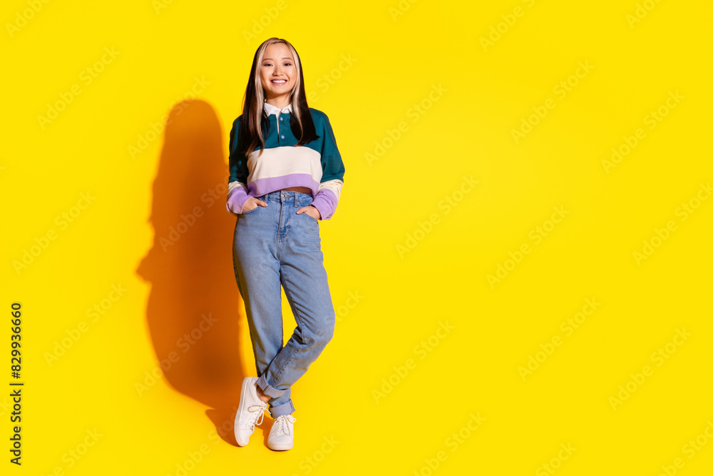 Full length photo of optimistic girl with dyed hair dressed striped shirt hold hands in pockets isolated on vivid yellow color background Full length photo of optimistic girl with dyed hair dressed striped shirt hold hands in pockets isolated on vivid yellow color background