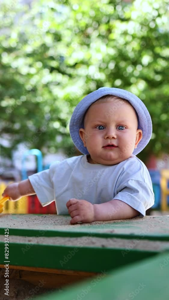 A cute blue-eyed boy of 11 months is playing in the sand on the street. A baby is playing in the sandbox on the playground A cute blue-eyed boy of 11 months is playing in the sand on the street. A baby is playing in the sandbox on the playground