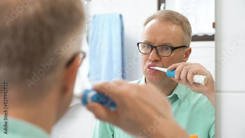 Middle-aged man brushing teeth with a electric brush in bathroom photo