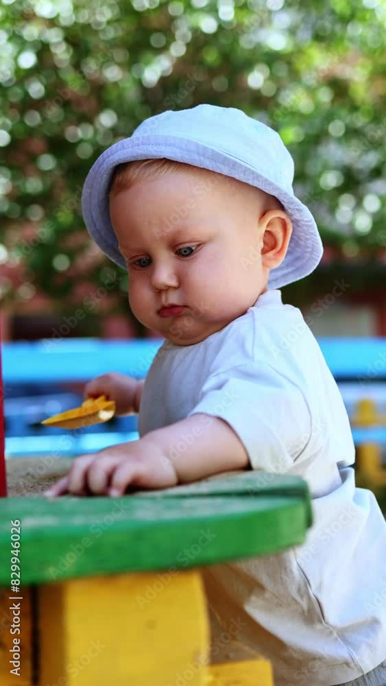 A cute blue-eyed boy of 11 months is playing in the sand on the street. A baby is playing in the sandbox on the playground A cute blue-eyed boy of 11 months is playing in the sand on the street. A baby is playing in the sandbox on the playground