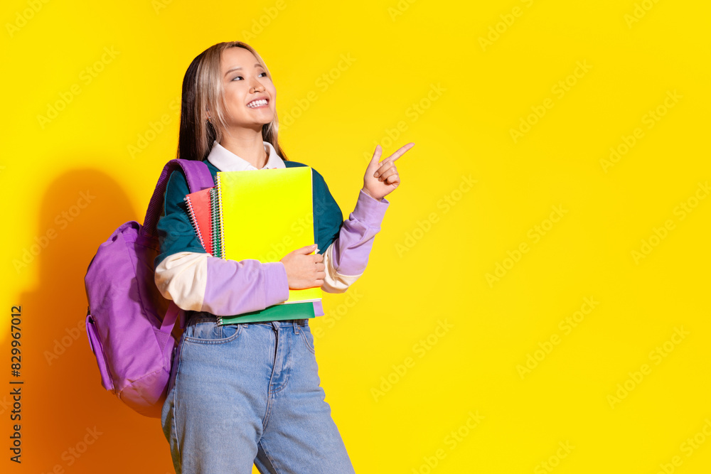 Photo of toothy beaming girl dressed striped shirt holding copybook look directing empty space isolated on yellow color background Photo of toothy beaming girl dressed striped shirt holding copybook look directing empty space isolated on yellow color background