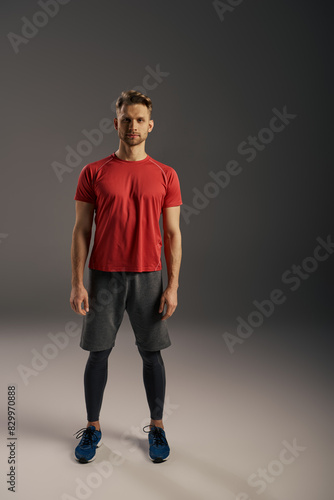A man in a red t-shirt and grey shorts confidently strikes a pose in front of a serene grey background. © LIGHTFIELD STUDIOS