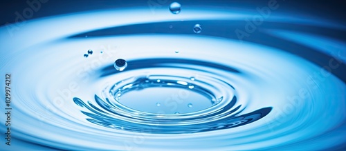 A blue water droplet falls into the water creating concentric circles and reflecting a blue wave Copy space image