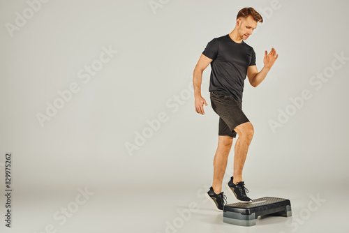 A young sportsman in active wear uses a stepper in a studio against a grey background.