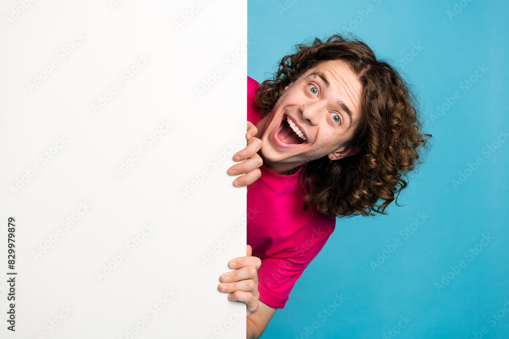 Portrait of ecstatic man with curly hair piercing wear pink shirt palms look out of wall empty space isolated on blue color background Portrait of ecstatic man with curly hair piercing wear pink shirt palms look out of wall empty space isolated on blue color background
