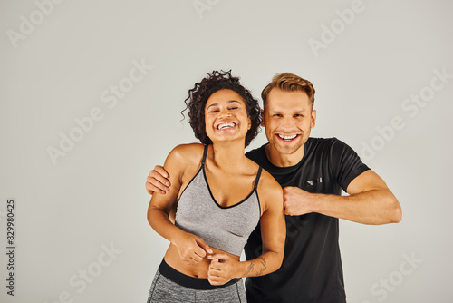 Fototapeta Naklejka Na Ścianę i Meble -  A young interracial sport couple in active wear confidently posing for the camera in a studio against a grey background.