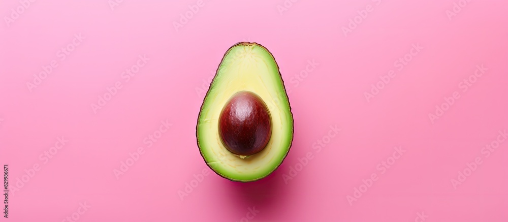 A fresh avocado seen from above rests on a pink background leaving ample room for other elements in the image A fresh avocado seen from above rests on a pink background leaving ample room for other elements in the image