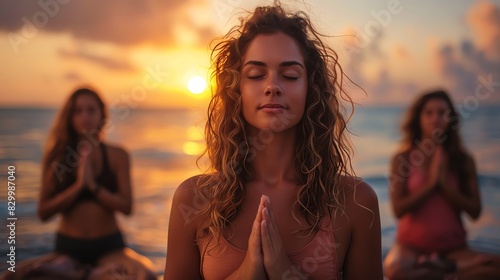 Three women meditating on the beach at sunset.