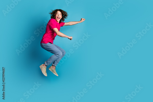 Full length portrait of nice young man jump empty space wear t-shirt isolated on blue color background