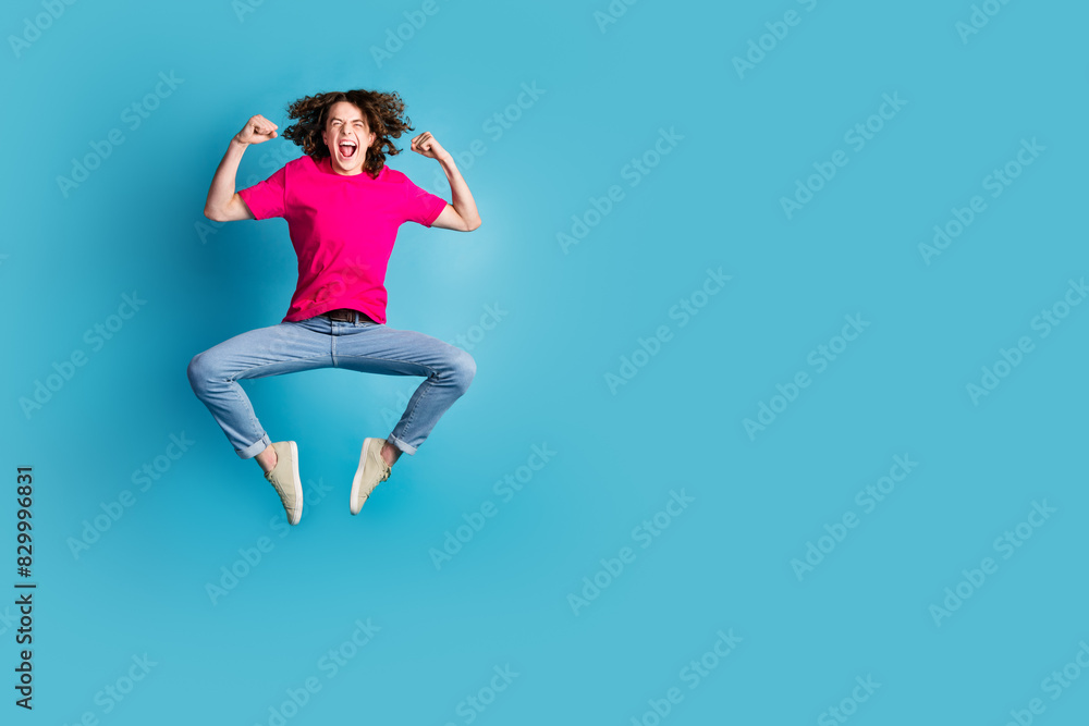 Full length portrait of nice young man jump raise fists wear t-shirt isolated on blue color background