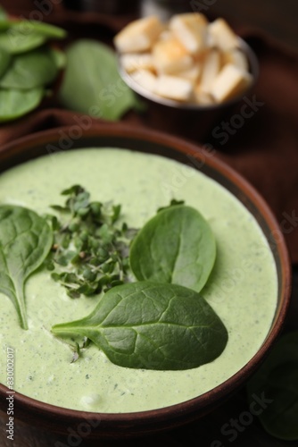 Delicious spinach cream soup with fresh leaves and microgreens in bowl on wooden table, closeup
