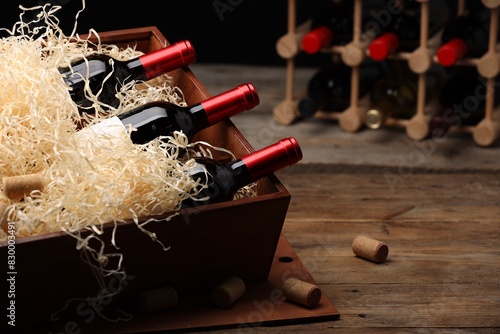 Box with wine bottles on wooden table against black background. Space for text