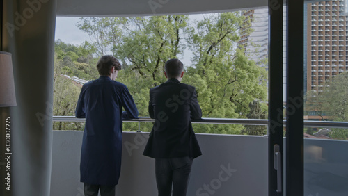 Rear view of two businessmen standing on the balcony and communicating. Stock clip. Men in hotel room at informal meeting.