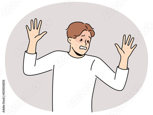 Frightened man raises hands in surrender and demonstrates obedience and refusal to resist. Frightened guy experiencing panic attack due to phobia associated with psychological trauma