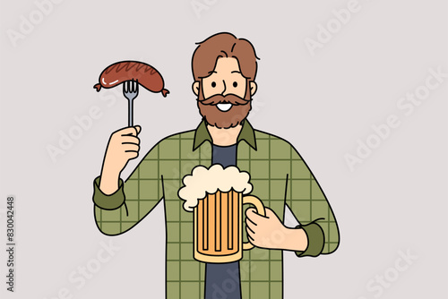 Man with mug of beer in hands and Bavarian sausage smiles, visiting pub or tavern to relax after working week. Happy guy participating in oktoberfest enjoying taste of foamy beer and meat snacks