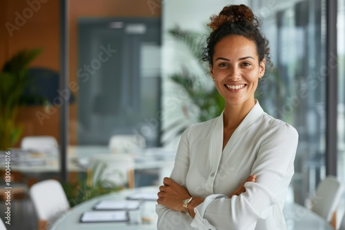 A portrait of a successful woman boss inside the office in a business suit shows a businesswoman smiling and looking at the camera, standing with crossed arms.
