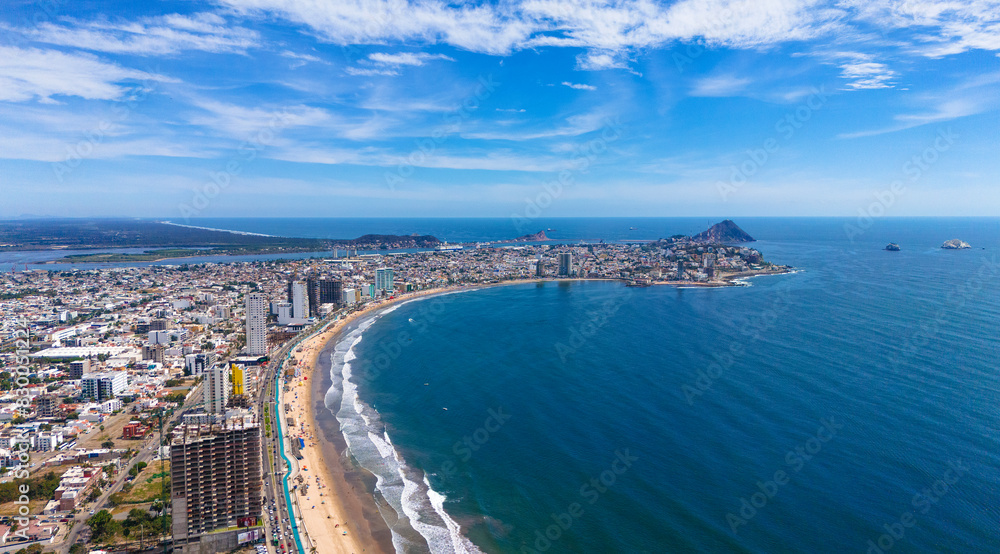 An aerial view of Mazatlán Beach on a sunny morning, showcasing the blue ocean's gentle waves meeting the sandy shores of this popular tourist destination An aerial view of Mazatlán Beach on a sunny morning, showcasing the blue ocean's gentle waves meeting the sandy shores of this popular tourist destination