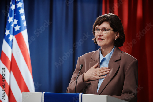 Mature female candidate for president post keeping hand on chest and looking at electorate while speaking in microphone photo
