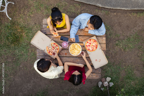 Four young asian friends enjoying pizza and drinks during an outdoor picnic in a lush garden or lawn. Top view looking down. photo