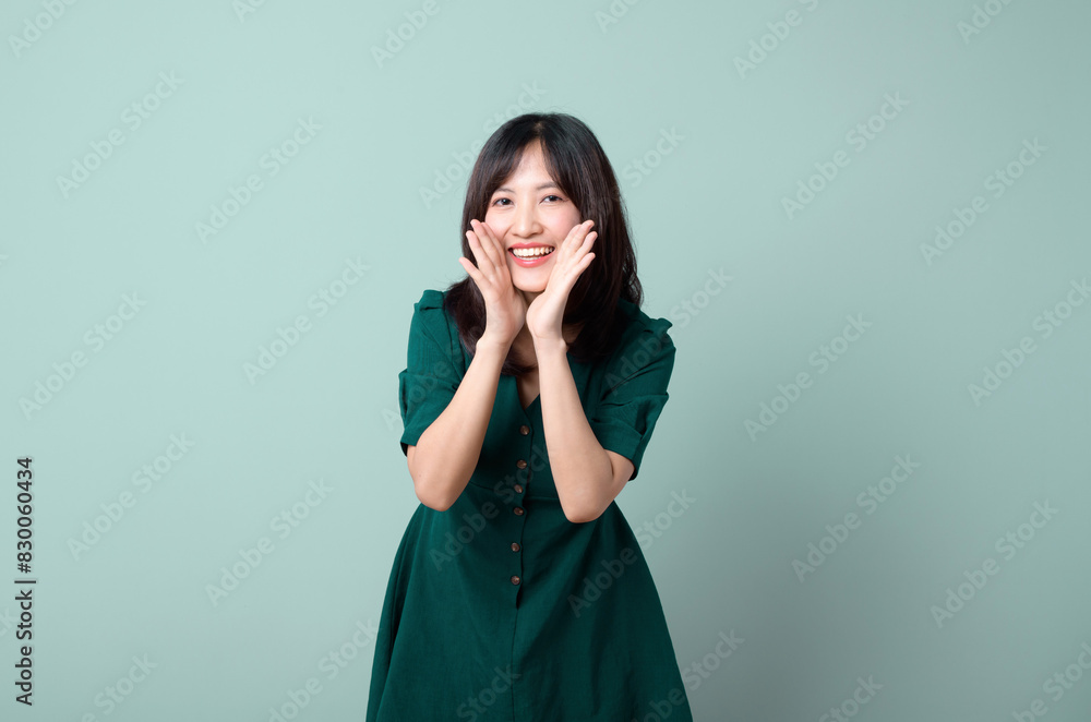 Happy Asian woman shouting above green dress poses against green background blank copy space for advertising content promotion Happy Asian woman shouting above green dress poses against green background blank copy space for advertising content promotion
