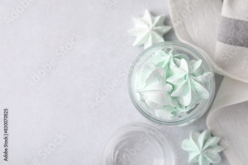 Tasty meringue cookies in glass jar on light grey table  top view. Space for text