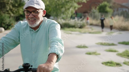 Cheerful hispanic senior man having fun riding bicycle at city park. healthy lifestyle