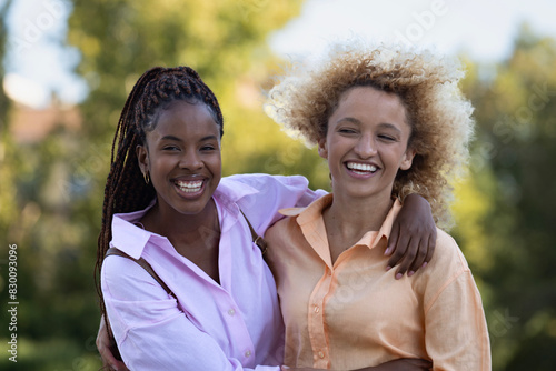 Two multiethnic women friends smiling and hugging each other in a park.