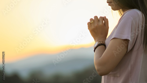 young woman clasped her hands together in prayer asking for forgiveness from God based on her Christian beliefs and faith in God teachings. concept prayer and intercession according beliefs about God