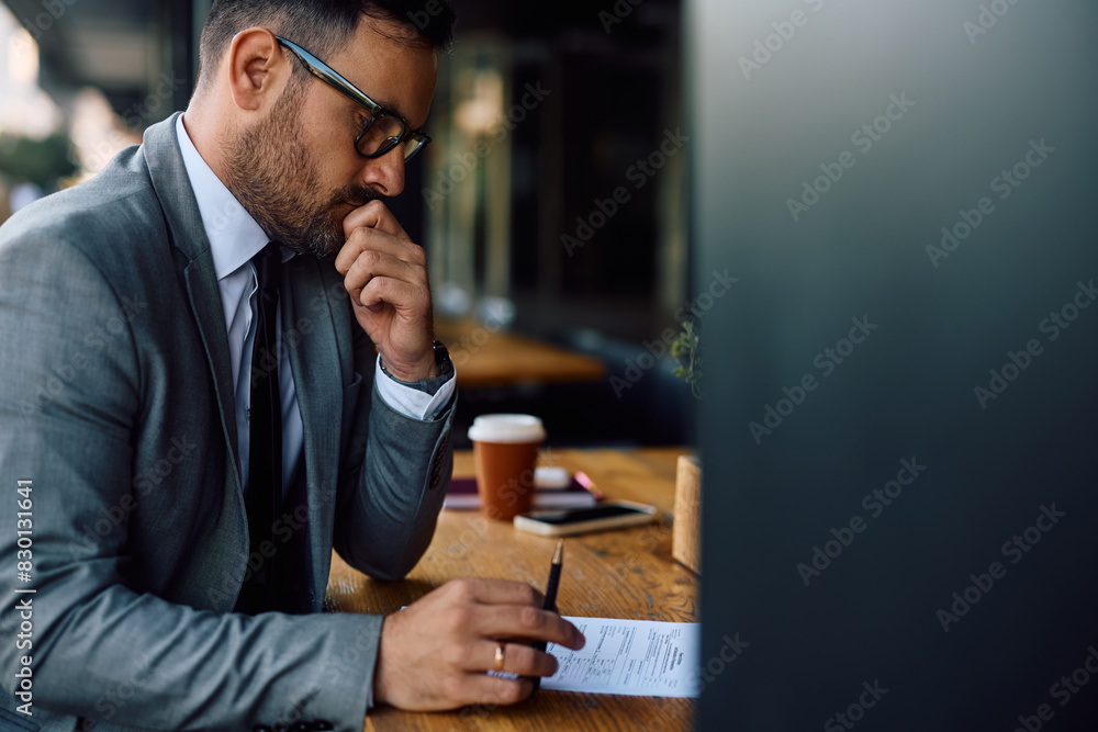 Thoughtful businessman going through paperwork while sitting in café. Thoughtful businessman going through paperwork while sitting in café.