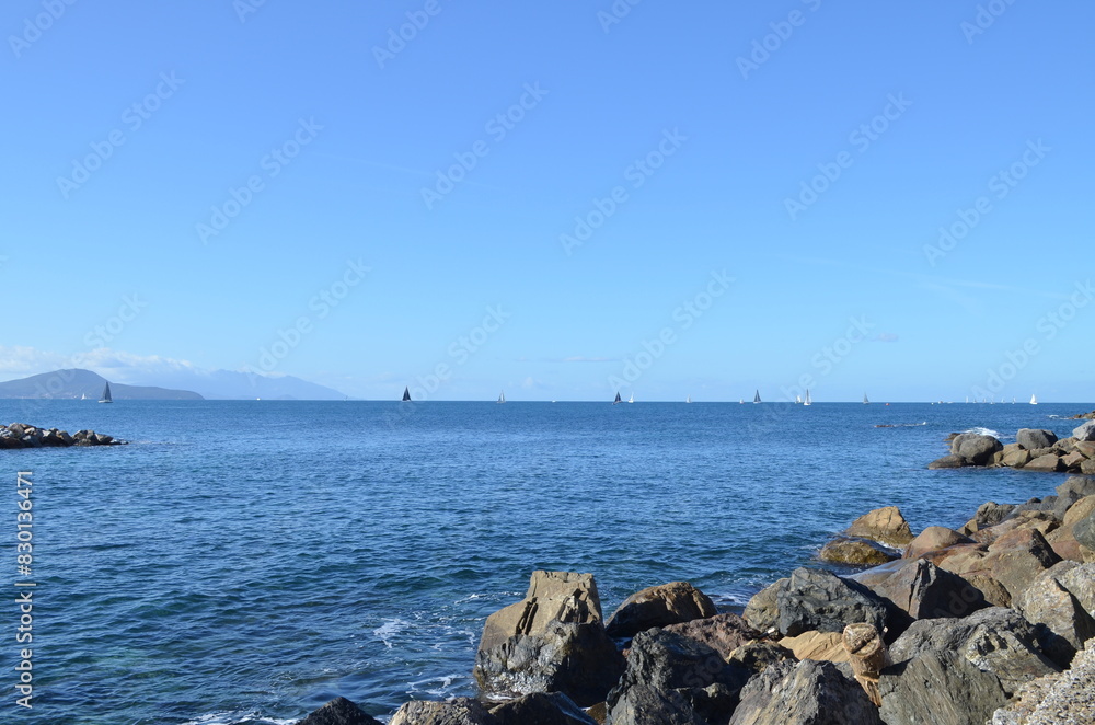 Black stones on the seashore, sailboats in the distance. Black stones on the seashore, sailboats in the distance.