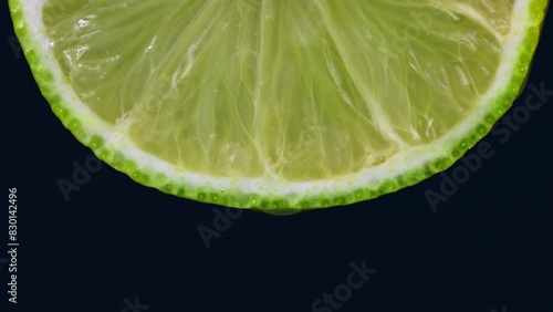 Transparent gel drop falling down from bright green lime slice on black background close up