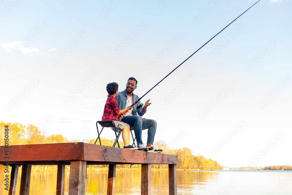 african american father and son fishing in the lake and sitting on wooden pier and holding fishing rod outdoors in summer, man teaches child to fish and relax outdoors on river african american father and son fishing in the lake and sitting on wooden pier and holding fishing rod outdoors in summer, man teaches child to fish and relax outdoors on river