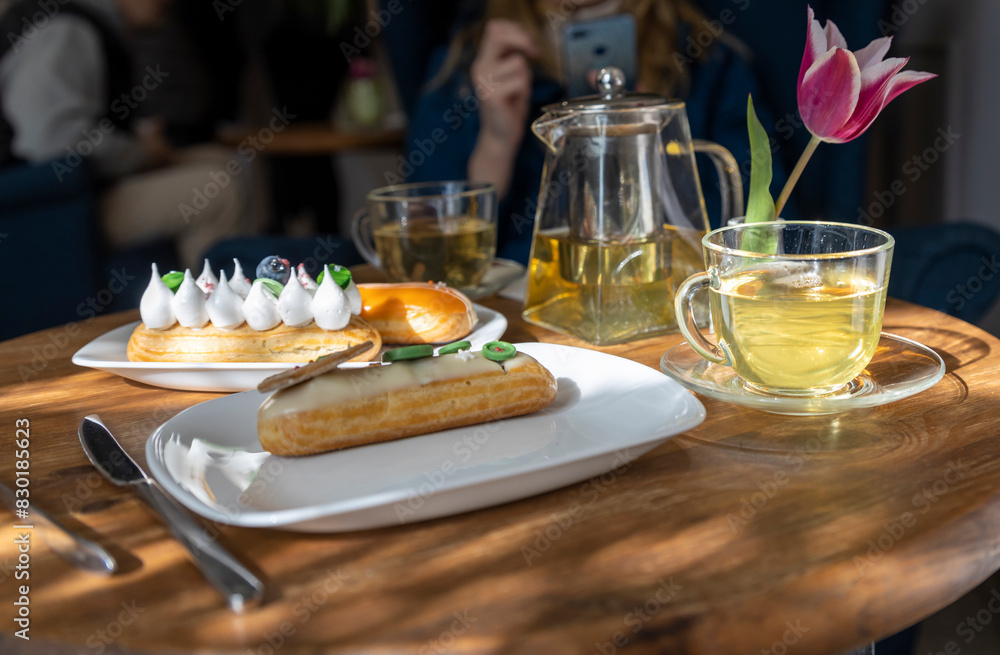 A cozy café scene features a wooden table adorned with pastries, a teapot, cups, and a striking pink tulip, creating an inviting atmosphere for leisurely dining and socializing A cozy café scene features a wooden table adorned with pastries, a teapot, cups, and a striking pink tulip, creating an inviting atmosphere for leisurely dining and socializing
