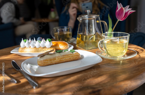 A cozy caf     scene features a wooden table adorned with pastries  a teapot  cups  and a striking pink tulip  creating an inviting atmosphere for leisurely dining and socializing