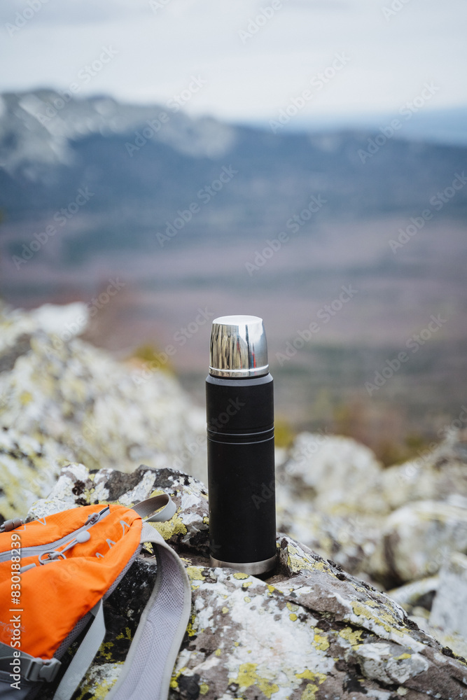 Thermos rests on rock near backpack in mountain landscape under sky Thermos rests on rock near backpack in mountain landscape under sky