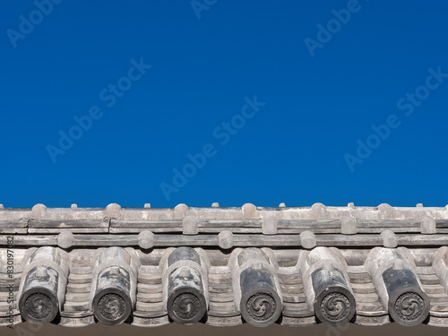 Japanese traditional grey roof tile with old spiral motif and blue sky above as background (with copy space)