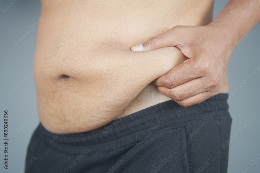 Naklejka premium man's hand holding excessive belly fat, overweight concept