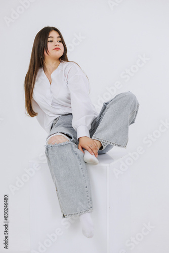 Photography A woman is sitting on a white box with ripped jeans