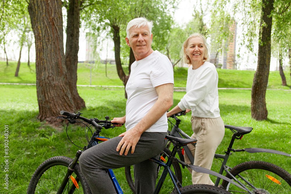 Obraz premium elderly senior couple rides bicycle in the park in the summer and smiles, old gray-haired man and woman are actively resting outdoors, old people practice cycling in forest