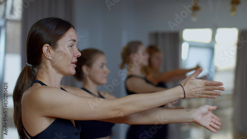 Group of sportive people during a gym training with a coach. Media. Girls group of athletes swinging hands before starting a workout yoga session.