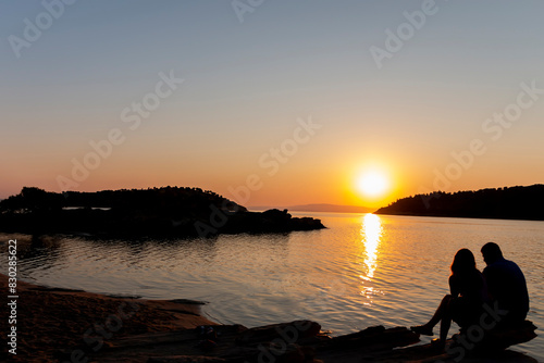 As the sun dips below the horizon, casting a warm orange glow across the sky, a striking silhouette emerges on the beach and couple.