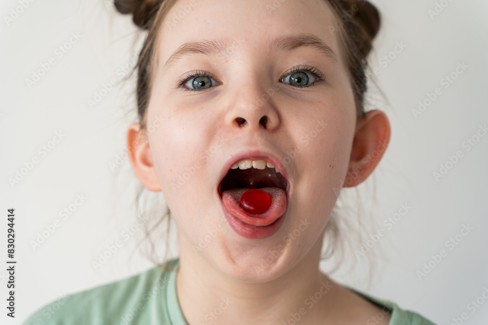 Cheerful little girl holding a pill in her mouth, a red lollipop. Easy treatment of the throat. Cheerful little girl holding a pill in her mouth, a red lollipop. Easy treatment of the throat.