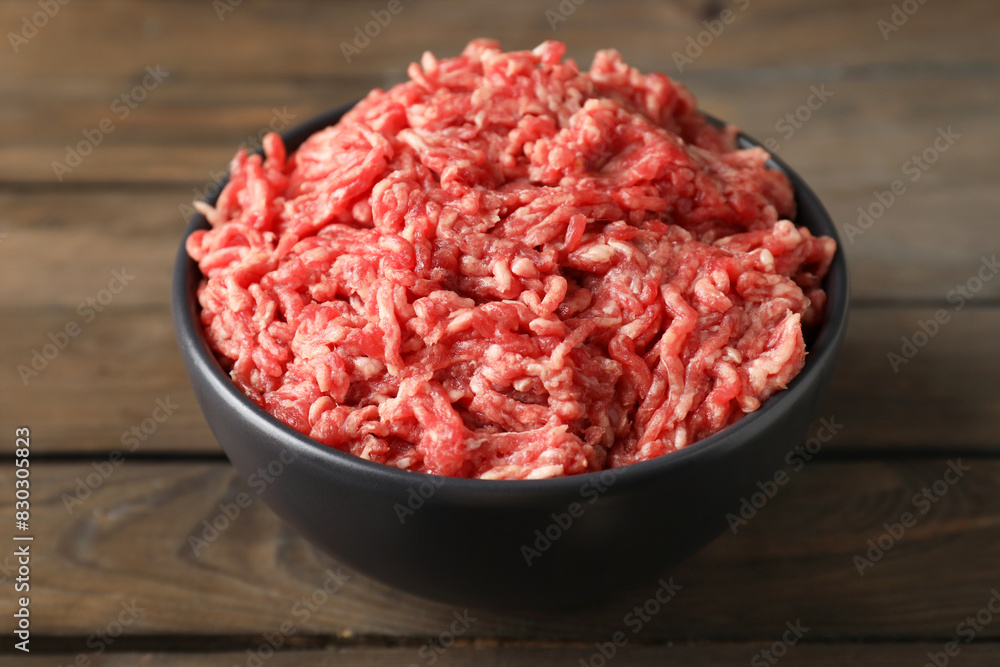 Raw ground meat in bowl on wooden table, closeup Raw ground meat in bowl on wooden table, closeup