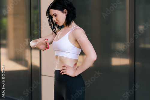 A woman doing fitness and uses a smart watch to measure the pulse on the hands. A woman does sports on the street. Fitness and a healthy lifestyle.   photo