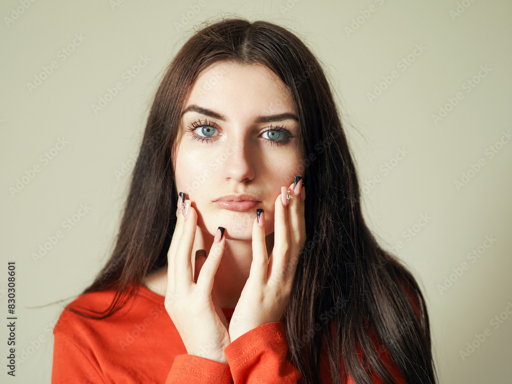 Portrait of a young teenager girl in red shirt on light color background. Model with long rich hair. Hands frame her face. Calm face expression. Beauty image. Portrait of a young teenager girl in red shirt on light color background. Model with long rich hair. Hands frame her face. Calm face expression. Beauty image.