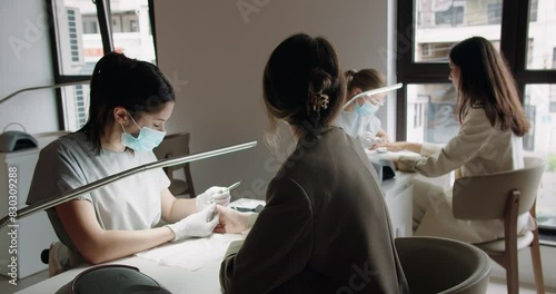 A manicurist treats a woman's cuticles using a manicure machine in a nail salon under the supervision of a teacher who processes a nail with nail scissors. Hand care procedures. photo