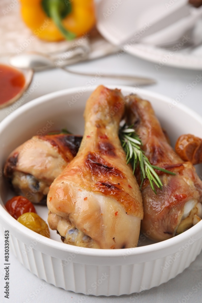 Delicious roasted chicken drumsticks with rosemary and tomatoes in bowl on white table, closeup Delicious roasted chicken drumsticks with rosemary and tomatoes in bowl on white table, closeup