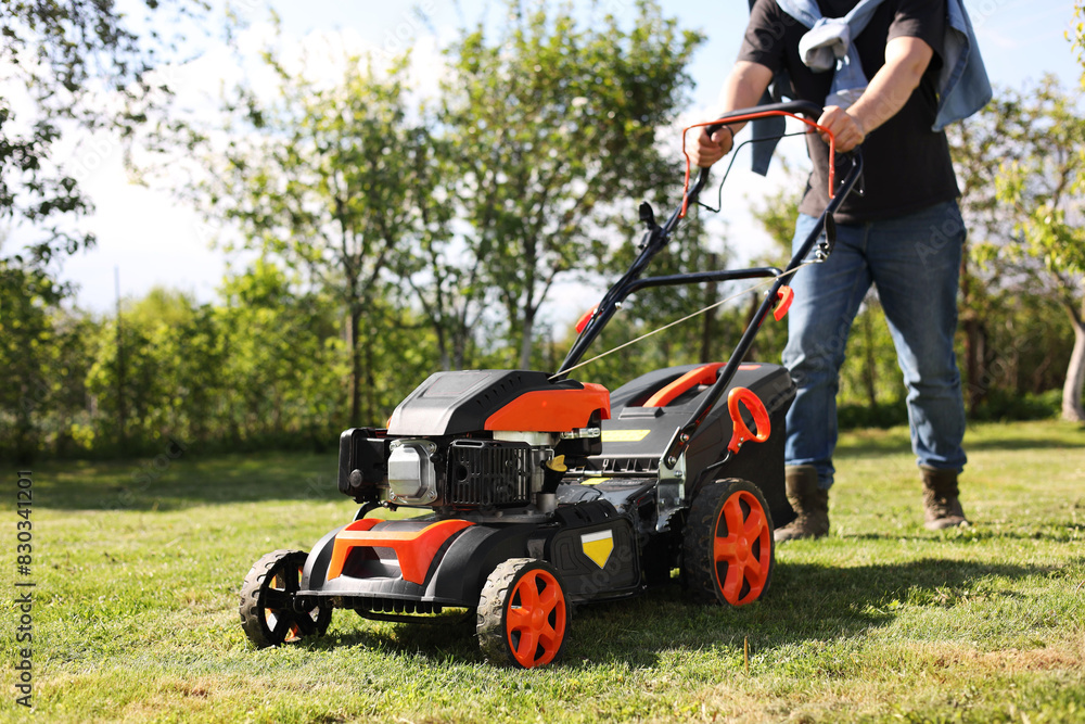 Man cutting green grass with lawn mower in garden, selective focus Man cutting green grass with lawn mower in garden, selective focus